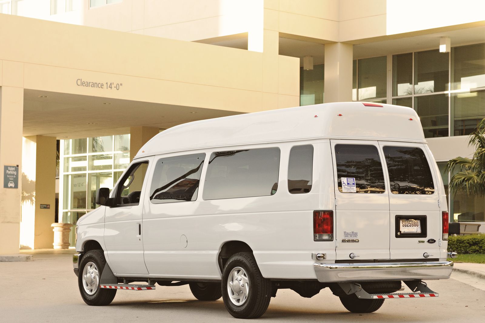 A large white passenger van parked in front of a modern office building entrance.